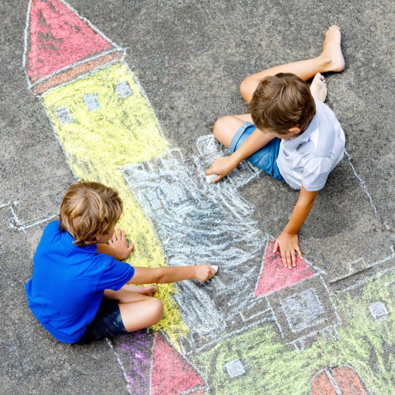 Two little kids boys drawing knight castle with colorful chalks on asphalt. Happy siblings and friends having fun with creating chalk picture and painting. Creative leisure for children in summer