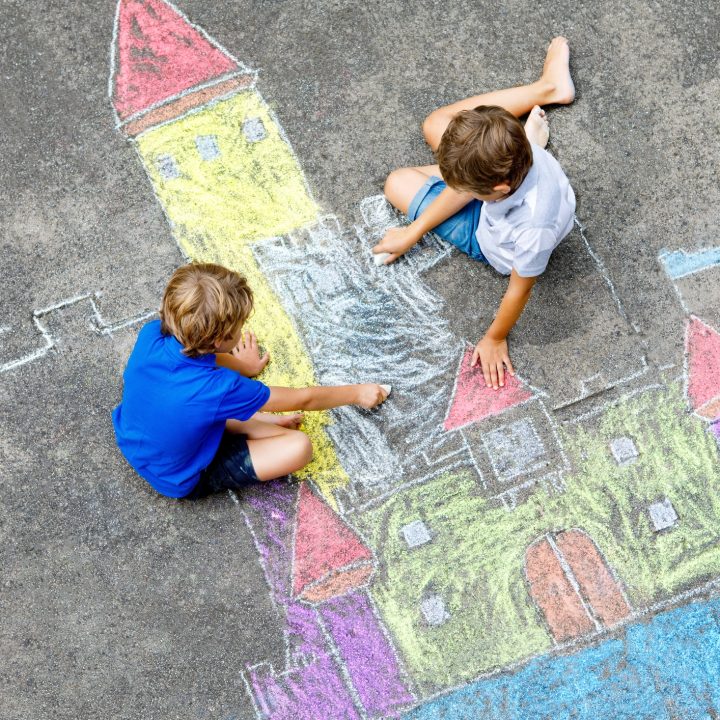 Two little kids boys drawing knight castle with colorful chalks on asphalt. Happy siblings and friends having fun with creating chalk picture and painting. Creative leisure for children in summer